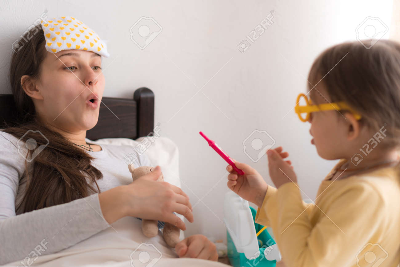 Cute little girl wearing uniform playing doctor or nurse with young mum or nanny in bedroom, checking mother throat, measures temperature, family spending leisure time at home together, role play game - 167137523 Cute little girl wearing uniform playing doctor or nurse with young mum or nanny in bedroom, checking mother throat, measures temperature, family spending leisure time at home together, role play game - 167137523