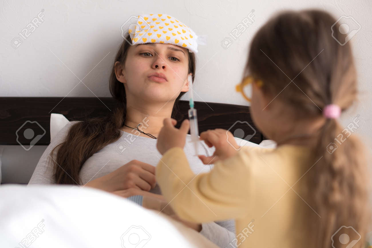 Cute little girl wearing uniform playing doctor or nurse with young mum or nanny in bedroom, makes an injection, measures temperature, family spending leisure time at home together, role play game - 167137544 Cute little girl wearing uniform playing doctor or nurse with young mum or nanny in bedroom, makes an injection, measures temperature, family spending leisure time at home together, role play game - 167137544