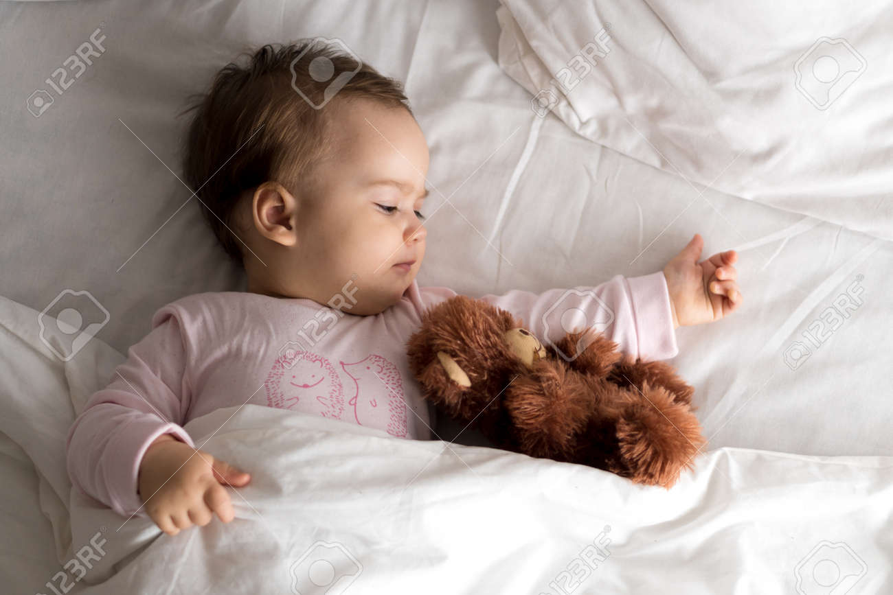 Authentic portrait cute caucasian little infant chubby baby girl or boy in pink sleepy upon waking with teddy bear looking at camera in white bed. Child care, Childhood, Parenthood, lifestyle concept - 167359907 Authentic portrait cute caucasian little infant chubby baby girl or boy in pink sleepy upon waking with teddy bear looking at camera in white bed. Child care, Childhood, Parenthood, lifestyle concept - 167359907