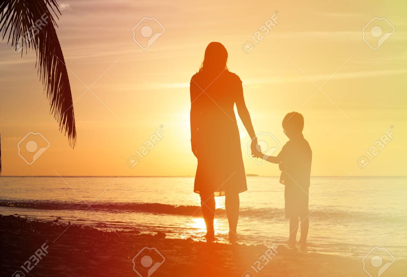 Silhouettes Of Mother And Son Holding Hands At Sunset Sea Stock
