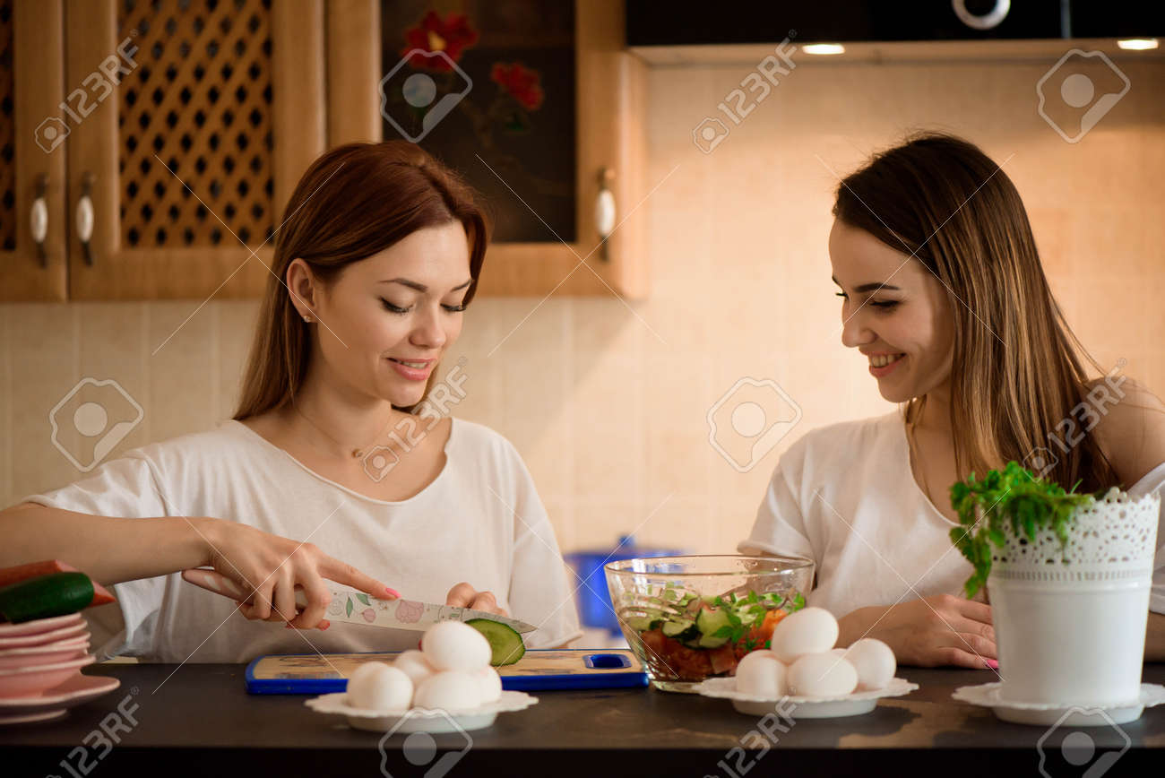 Young girlfriends chopping vegetables with twin in a family home kitchen. - 166330296 Young girlfriends chopping vegetables with twin in a family home kitchen. - 166330296