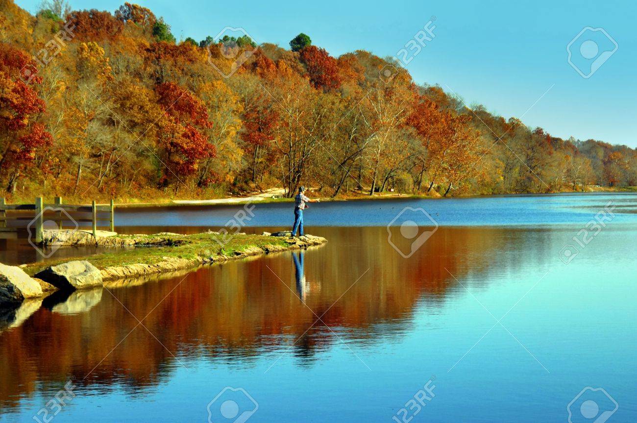 Lone fisherman casts his line into small lake in northern Arkansas Early morning light reflects blue into lake - 15024669 Lone fisherman casts his line into small lake in northern Arkansas Early morning light reflects blue into lake - 15024669