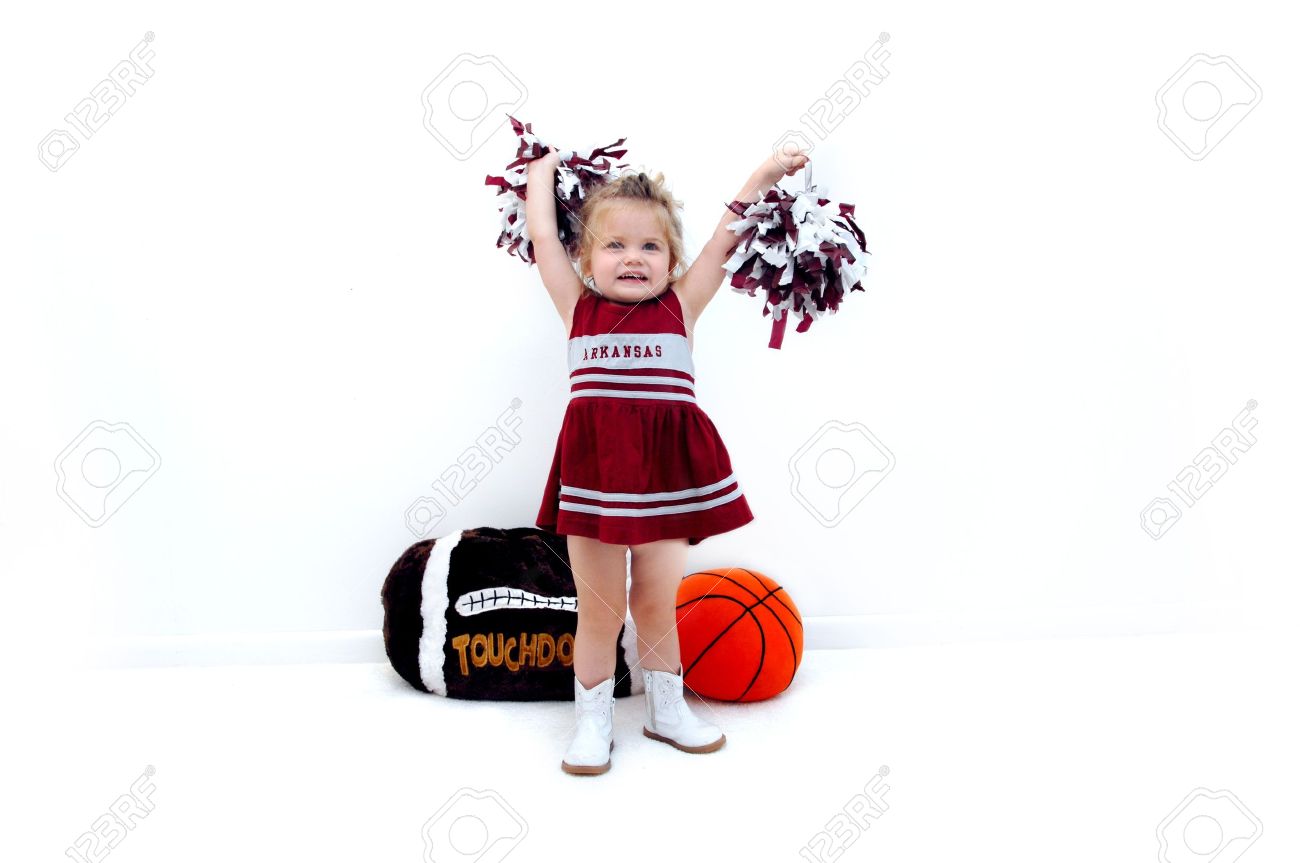 Little cheerleader dressed in burgundy and grey holds pom poms high in the air She is wearing white gogo boots and standing in front of a stuffed football and basketball - 15023628 Little cheerleader dressed in burgundy and grey holds pom poms high in the air She is wearing white gogo boots and standing in front of a stuffed football and basketball - 15023628