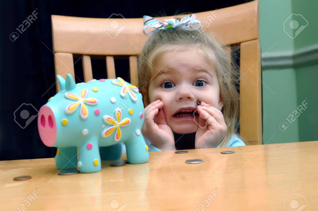 Little girl looks upset that she has to save all her pennies She is holding two against her cheek Brightly colored aqua piggy bank sits besides her at their kitchen table - 15023993 Little girl looks upset that she has to save all her pennies She is holding two against her cheek Brightly colored aqua piggy bank sits besides her at their kitchen table - 15023993