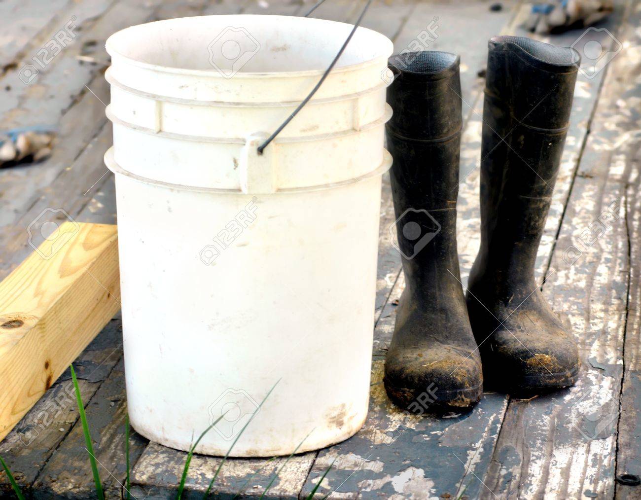 Muddy work boots set besides a five gallon bucket on a wooden porch Porch boards are cracked and peeling Work gloves lay in background Boots represent a work ethic - 15056430 Muddy work boots set besides a five gallon bucket on a wooden porch Porch boards are cracked and peeling Work gloves lay in background Boots represent a work ethic - 15056430