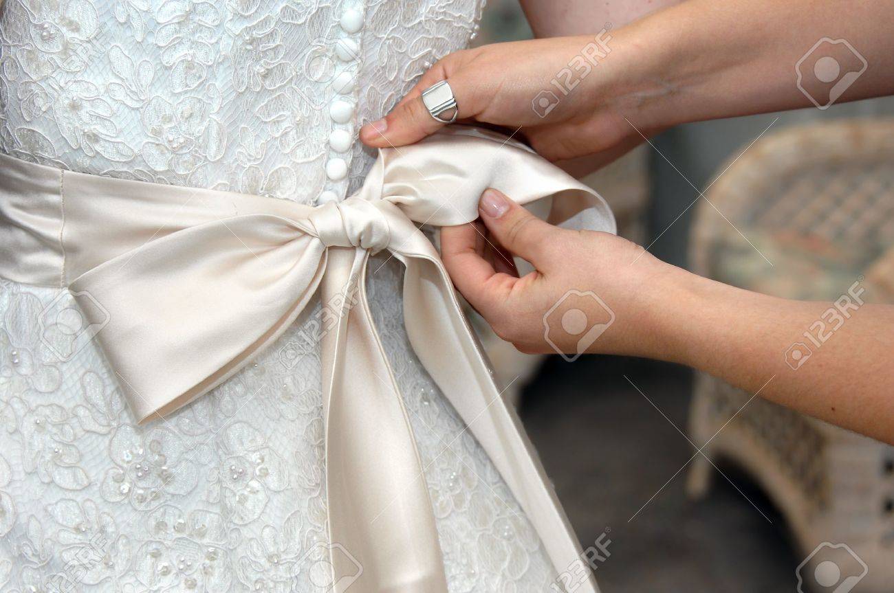 Hands tie the satin bow of wedding gown Closeup of female hands looping ties into elegant bow - 15104392 Hands tie the satin bow of wedding gown Closeup of female hands looping ties into elegant bow - 15104392