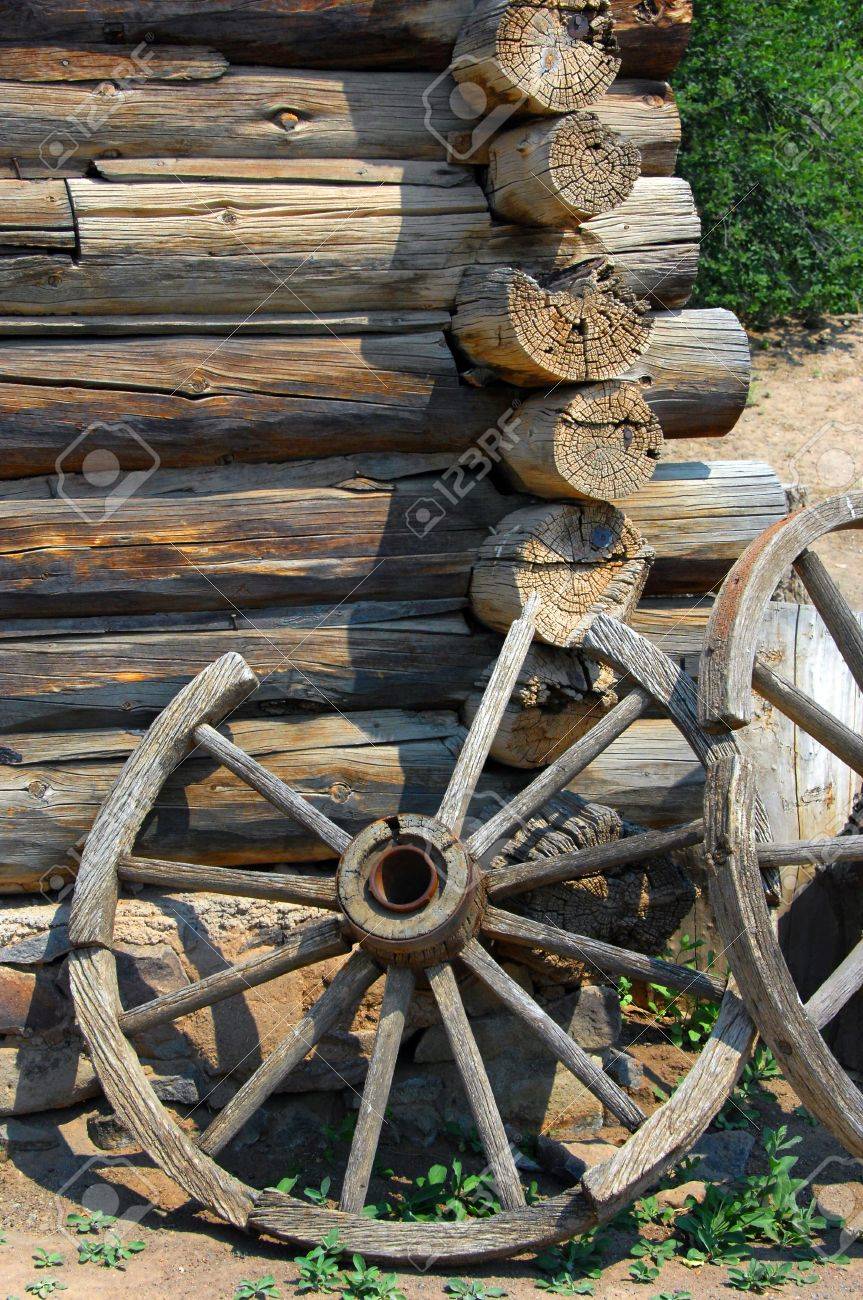 Two rustic wagon wheels lean against a log cabin wall at the El Rancho De Las Golondrinas National Historic Trail. - 15110810 Two rustic wagon wheels lean against a log cabin wall at the El Rancho De Las Golondrinas National Historic Trail. - 15110810