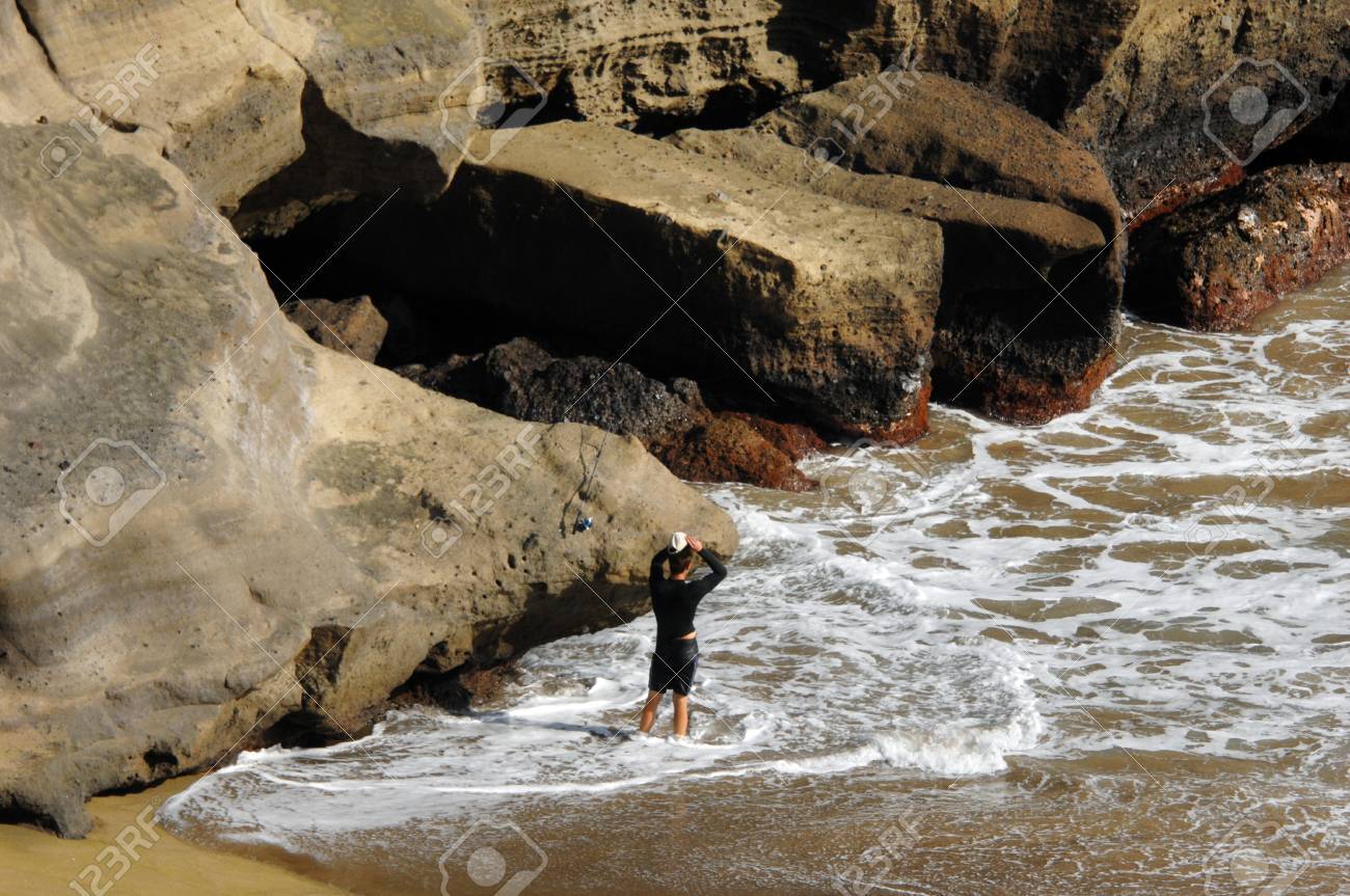 若い男性ハワイ島上有名な緑の砂のビーチの釣りのための準備で彼の帽子を身に付けた 巨大な崖は頑丈で 波や風によって浸食されました 崖のサイズが 小柄な男と比較して見られます の写真素材 画像素材 Image