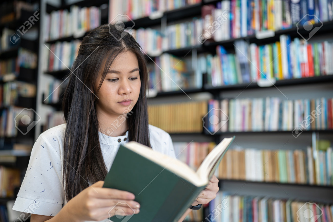 Asian woman is reading a book in the university library. - 165769694 Asian woman is reading a book in the university library. - 165769694