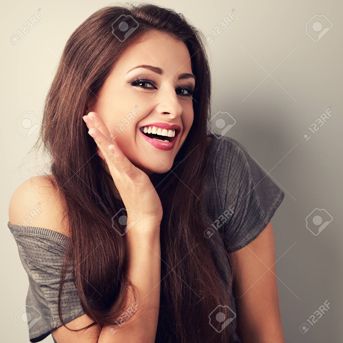 Happy toothy laughing brunette young woman with hand near face. Toned closeup portrait - 57057996 Happy toothy laughing brunette young woman with hand near face. Toned closeup portrait - 57057996