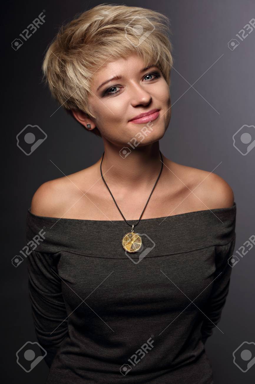 グレーのブラウスと灰色の背景にオレンジ色のファッション ネックレス ショート金髪ボブ髪型と幸せな笑顔の女性 ポートレート クローズ アップ の写真素材 画像素材 Image