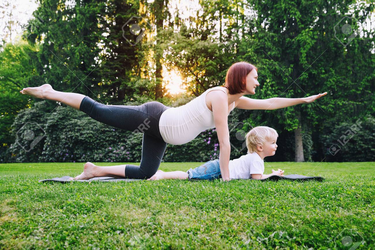 Beautiful pregnant woman doing yoga with little son on nature outdoors. Mother and cute toddler child doing sports exercises together and have fun in summer park. Little yogi, yoga kids. - 78979360 Beautiful pregnant woman doing yoga with little son on nature outdoors. Mother and cute toddler child doing sports exercises together and have fun in summer park. Little yogi, yoga kids. - 78979360