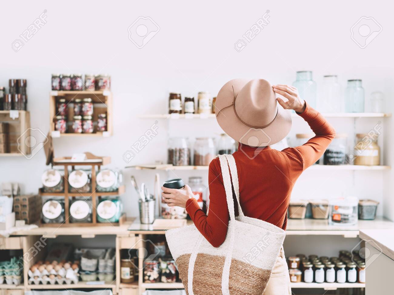 Minimalist vegan style girl with wicker bag and reusable glass coffee cup on background of interior of zero waste shop. Woman doing shopping without plastic packaging in plastic free grocery store. - 134621130 Minimalist vegan style girl with wicker bag and reusable glass coffee cup on background of interior of zero waste shop. Woman doing shopping without plastic packaging in plastic free grocery store. - 134621130