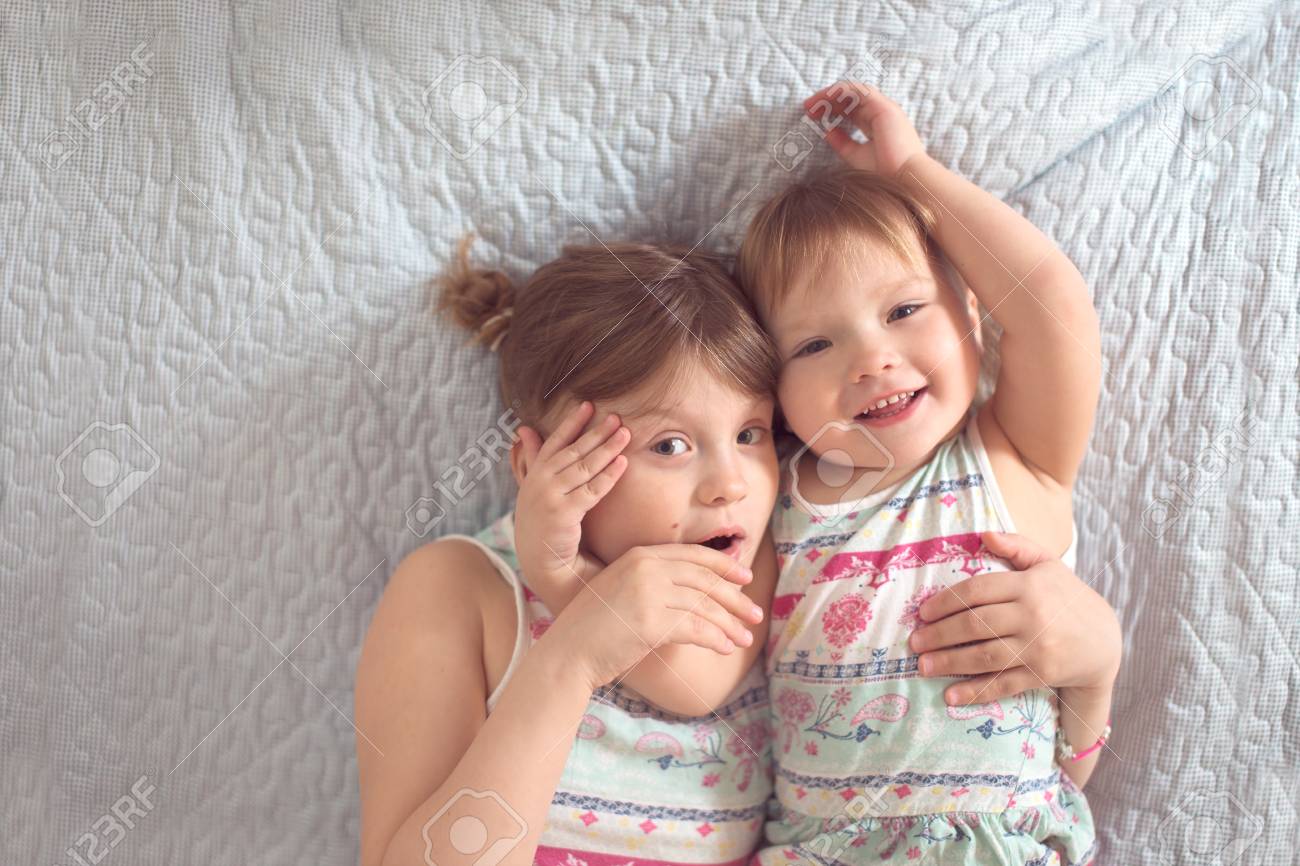 two cute siblings hugging and smiling on the bed light background