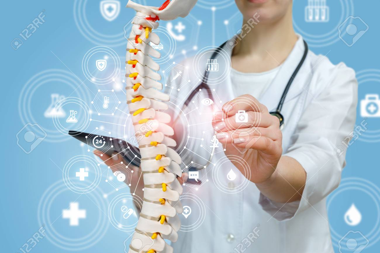 A closeup of doctor with stethoscope operating with artificial spine model holding a tablet in hand inside a medical service structure. The concept of innovative approach in spine diseases treatment. - 120976877 A closeup of doctor with stethoscope operating with artificial spine model holding a tablet in hand inside a medical service structure. The concept of innovative approach in spine diseases treatment. - 120976877