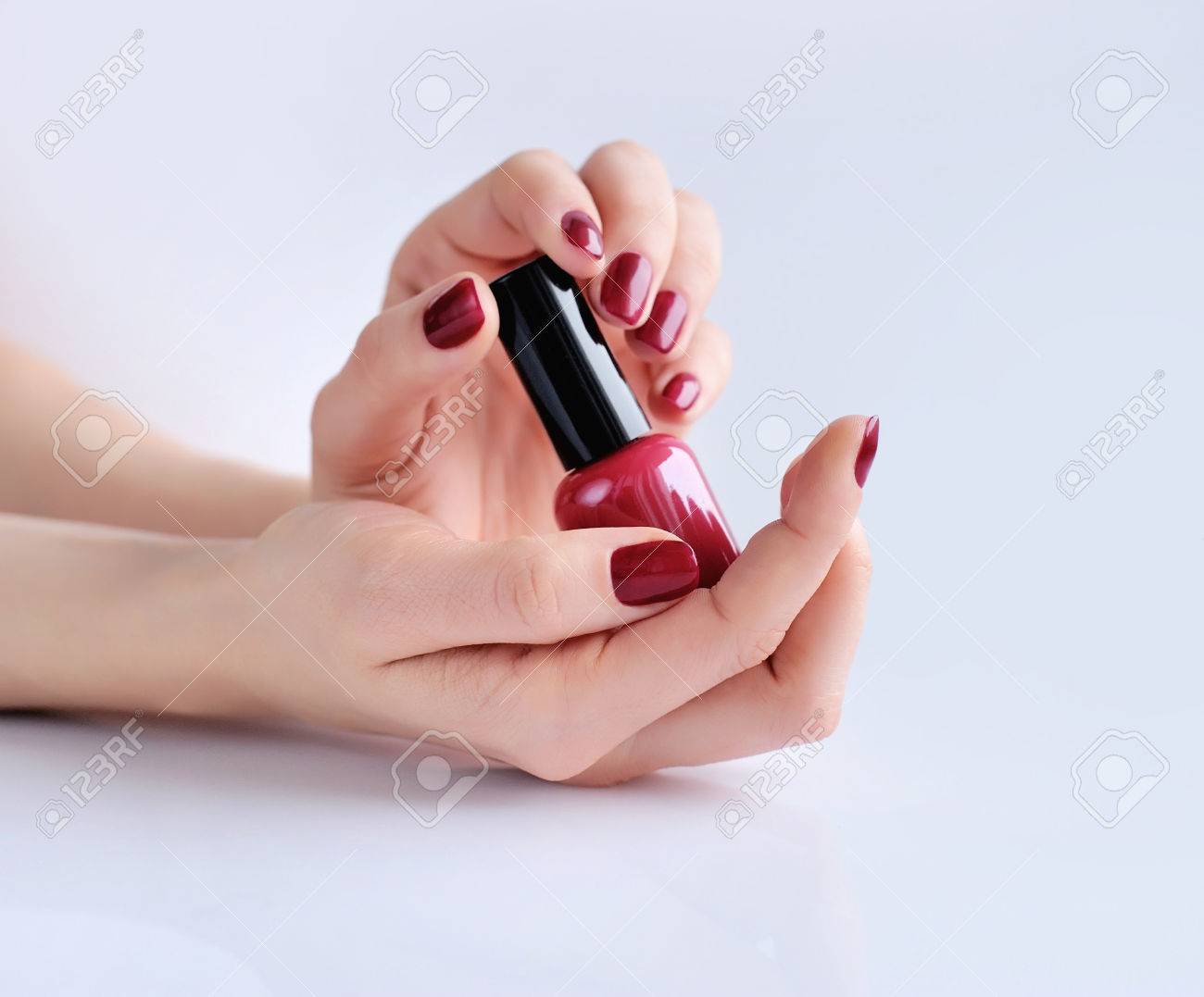 Hands Of A Woman With Dark Red Manicure And Nail Polish Bottle Stock