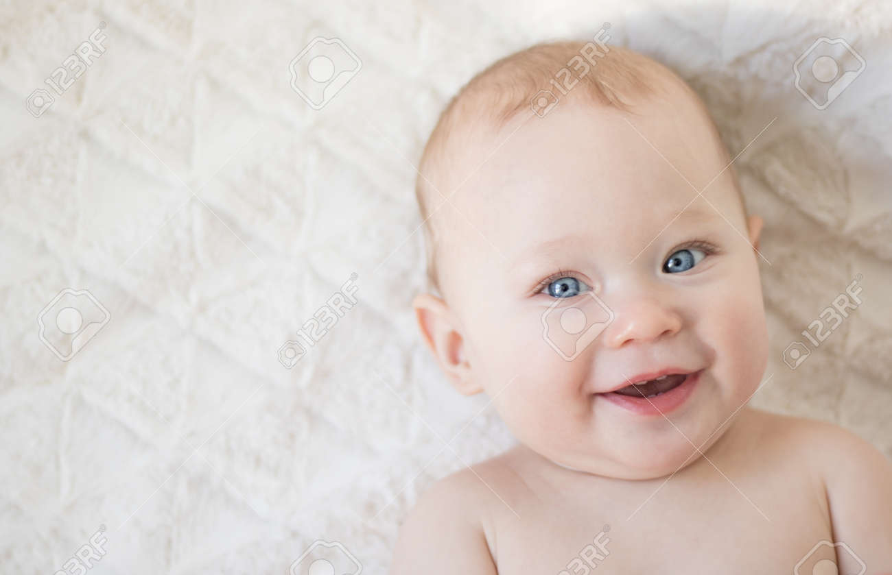 Cute little smiling baby girl face with blue eyes and light fair hairs on a soft plush bedcover. Top view, copy space for your text - 166495225 Cute little smiling baby girl face with blue eyes and light fair hairs on a soft plush bedcover. Top view, copy space for your text - 166495225