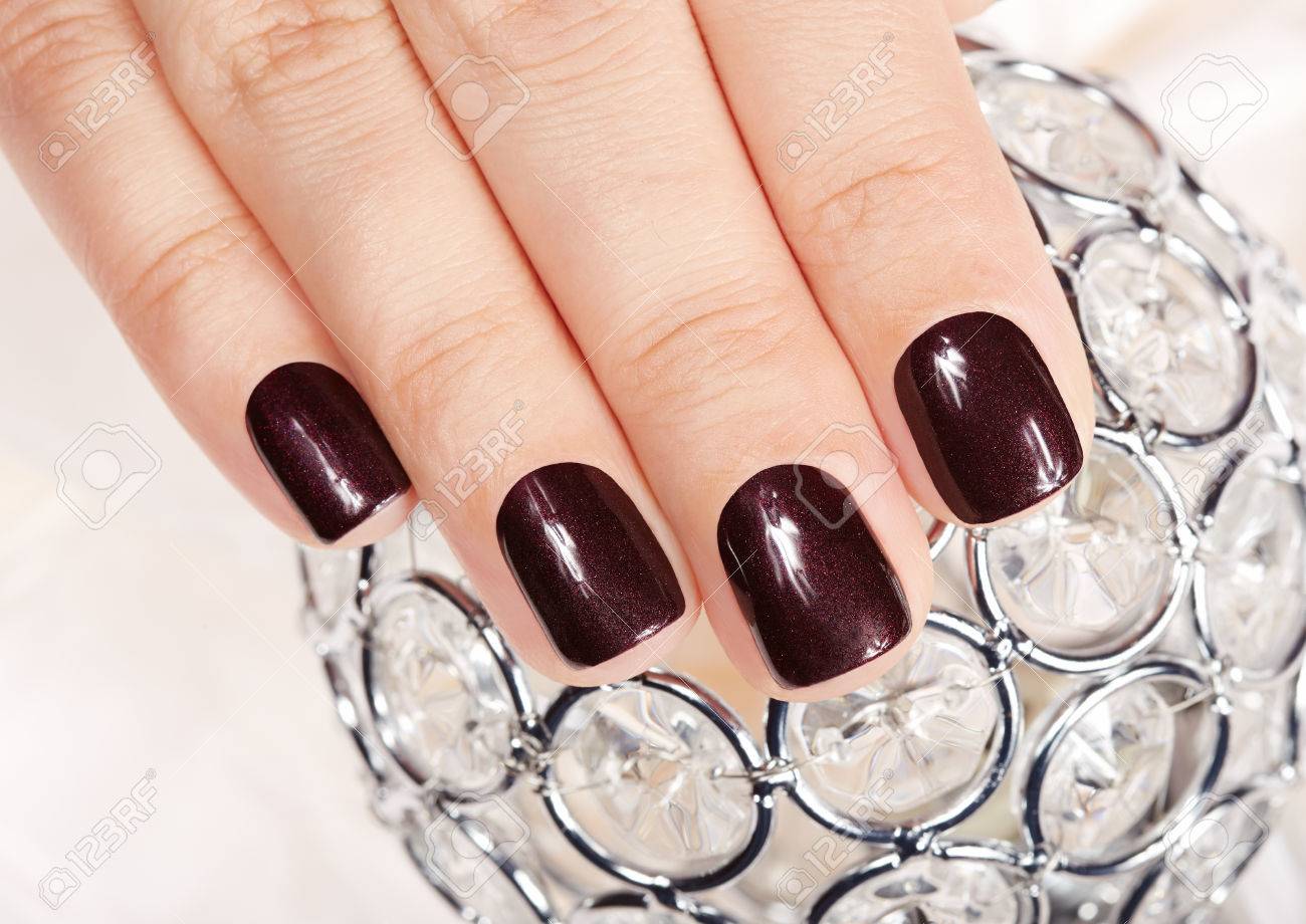 hand with short manicured nails colored with dark purple nail