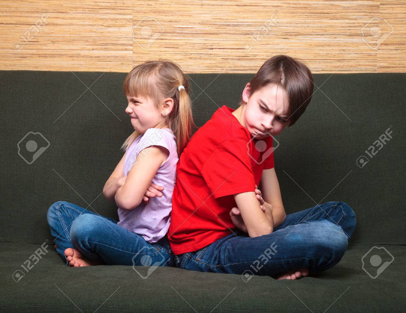 Brother and sister wearing casual clothes sitting on a green sofa at home arms crossed back to back angry with each other - 51199571 Brother and sister wearing casual clothes sitting on a green sofa at home arms crossed back to back angry with each other - 51199571