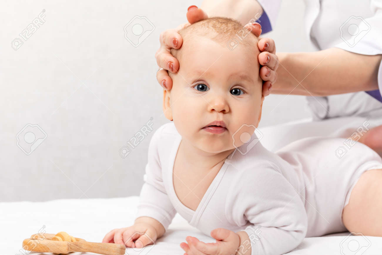 Six month baby girl receiving osteopathic or chiropractic treatment in pediatric clinic. Manual therapist manipulates chils's head and neck - 166892700 Six month baby girl receiving osteopathic or chiropractic treatment in pediatric clinic. Manual therapist manipulates chils's head and neck - 166892700