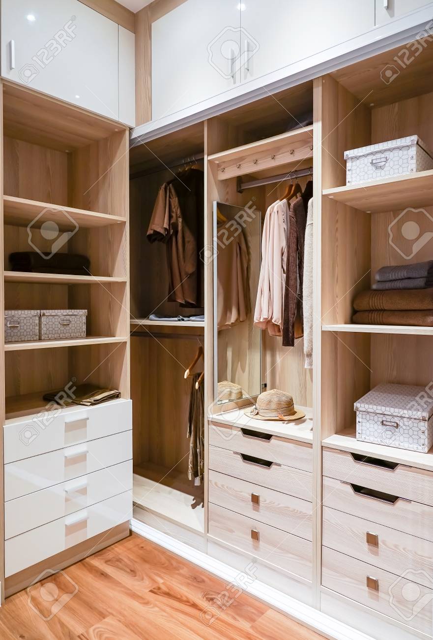 Modern Wooden Wardrobe With Clothes Hanging On Rail In Walk In