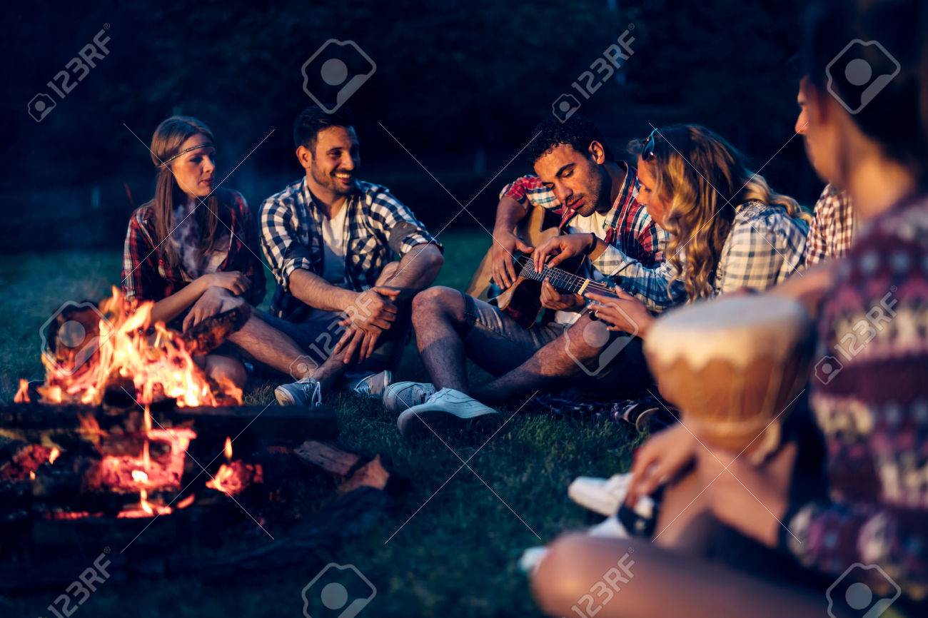 友人は夜キャンプファイヤーの近く音楽を楽しんで の写真素材 画像素材 Image