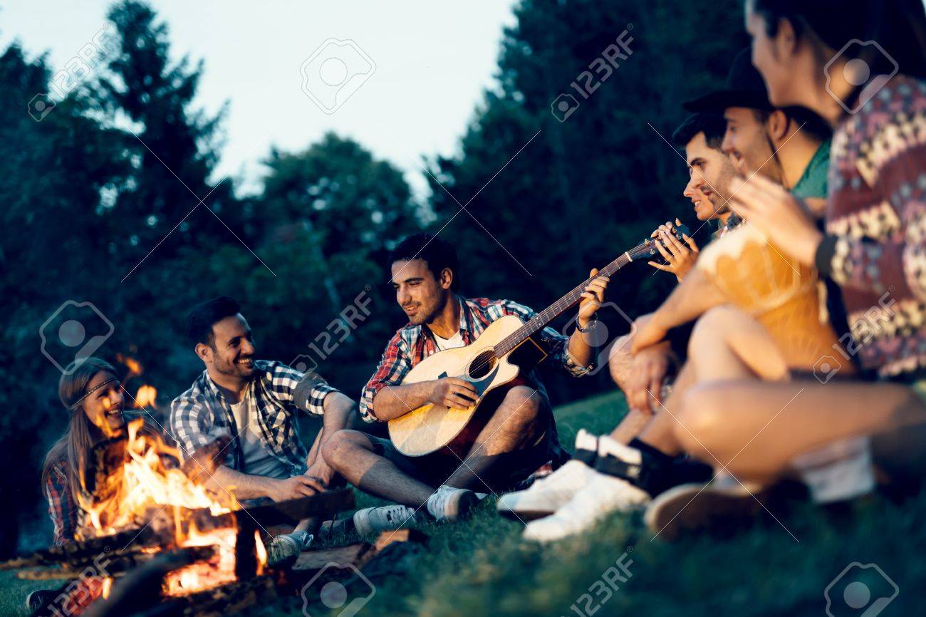 友人は夜キャンプファイヤーの近く音楽を楽しんで の写真素材 画像素材 Image