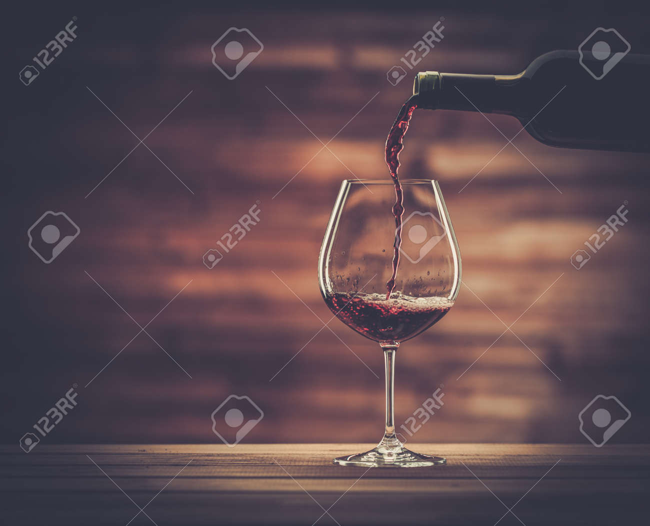 Pouring red wine into the glass against wooden background - 33958935 Pouring red wine into the glass against wooden background - 33958935