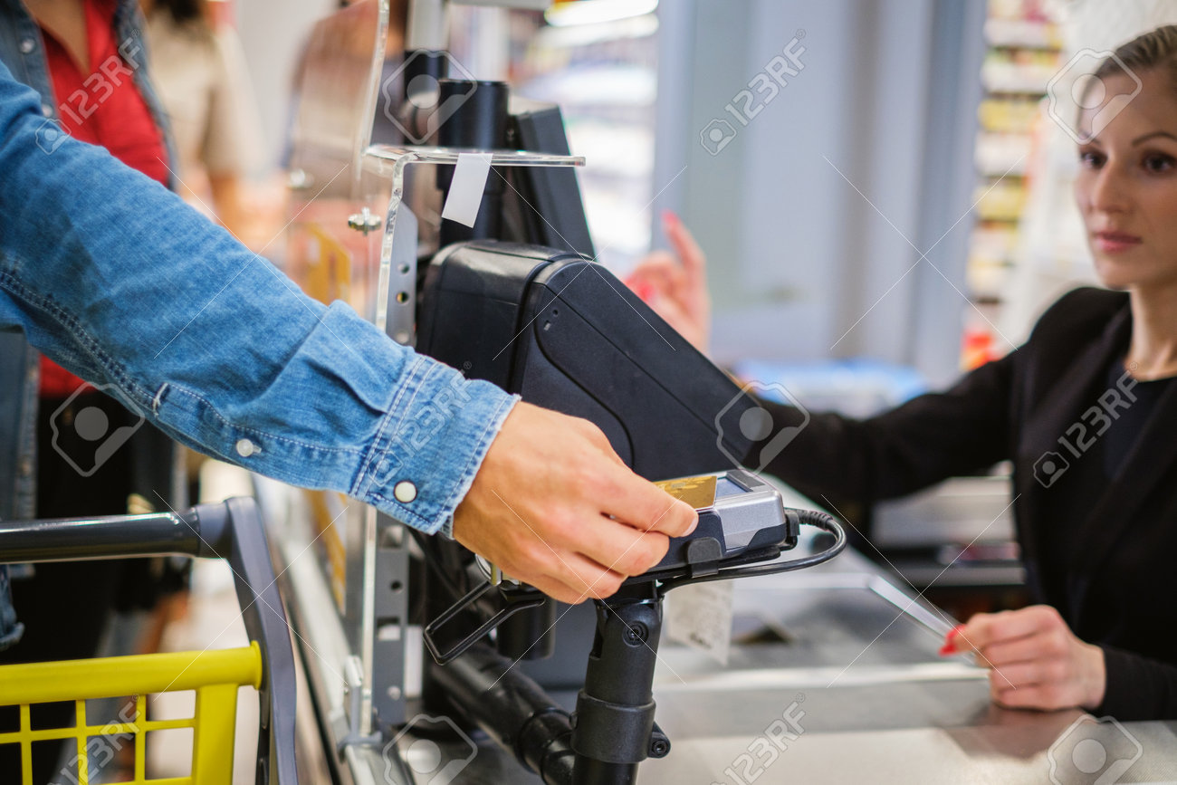 Man paying with a smartphone in a grocery store - 130993098 Man paying with a smartphone in a grocery store - 130993098