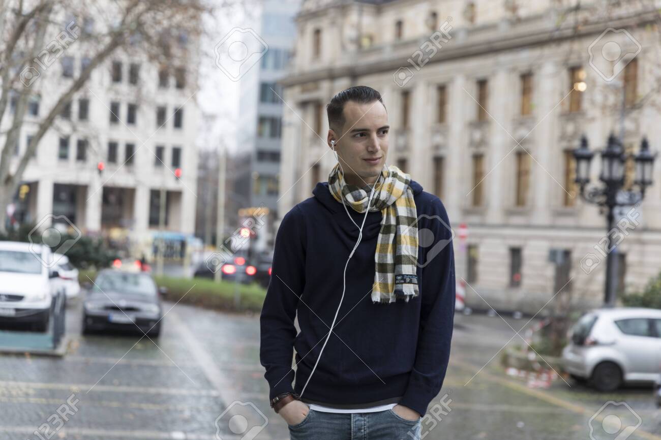 Young Man with Earphones and Head Turned in Urban Setting - 144008625 Young Man with Earphones and Head Turned in Urban Setting - 144008625