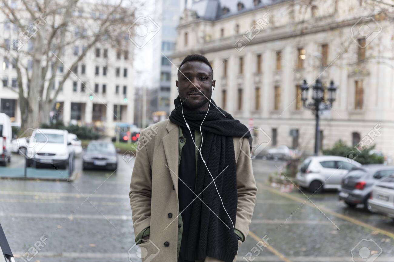 Young Black Man Wearing Beige Coat Posing in City - 146783184 Young Black Man Wearing Beige Coat Posing in City - 146783184
