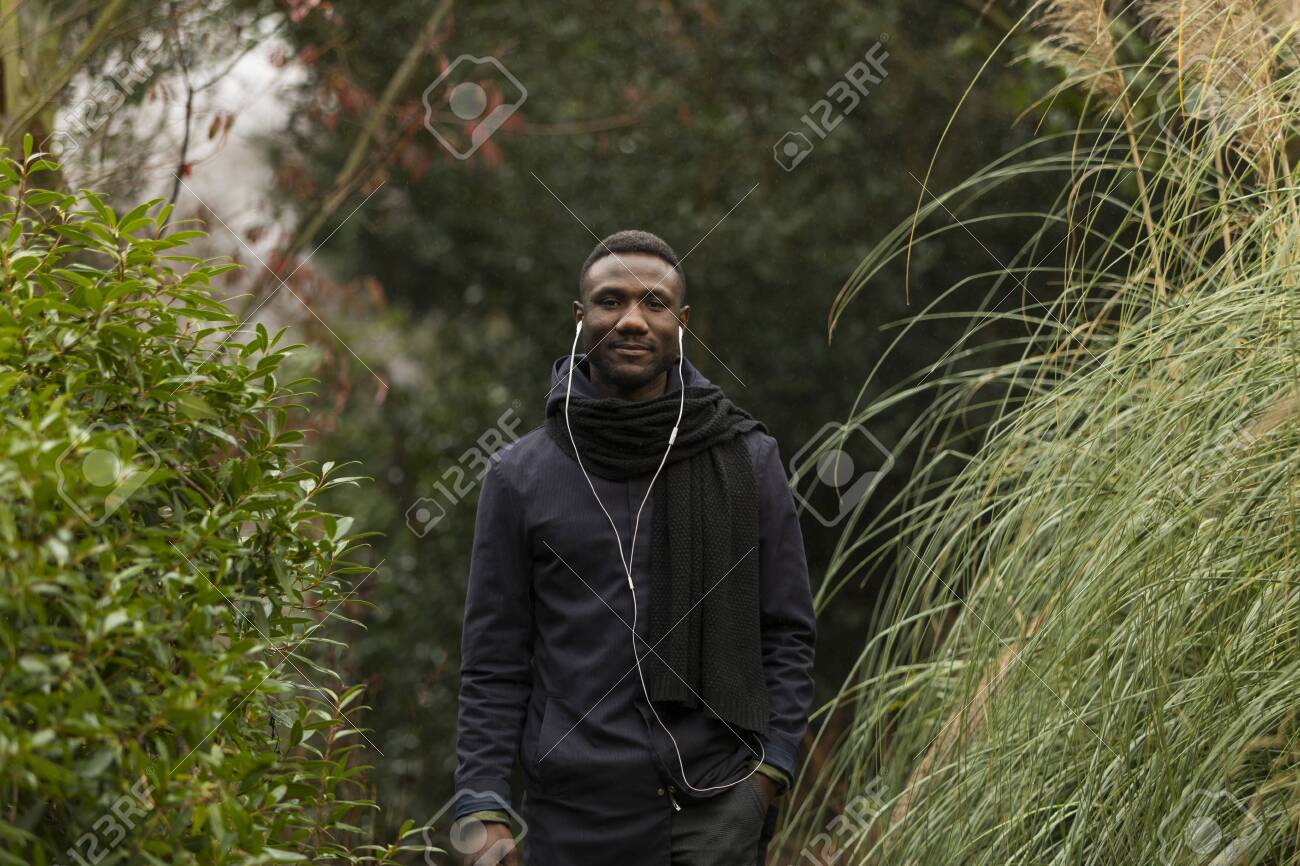 Young Man with Earphones Posing in Park - 146783204 Young Man with Earphones Posing in Park - 146783204