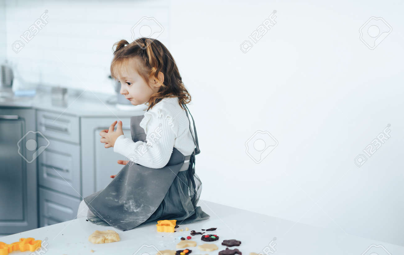 Little girl cooking sweet cookies, sitting on table. - 169694078 Little girl cooking sweet cookies, sitting on table. - 169694078