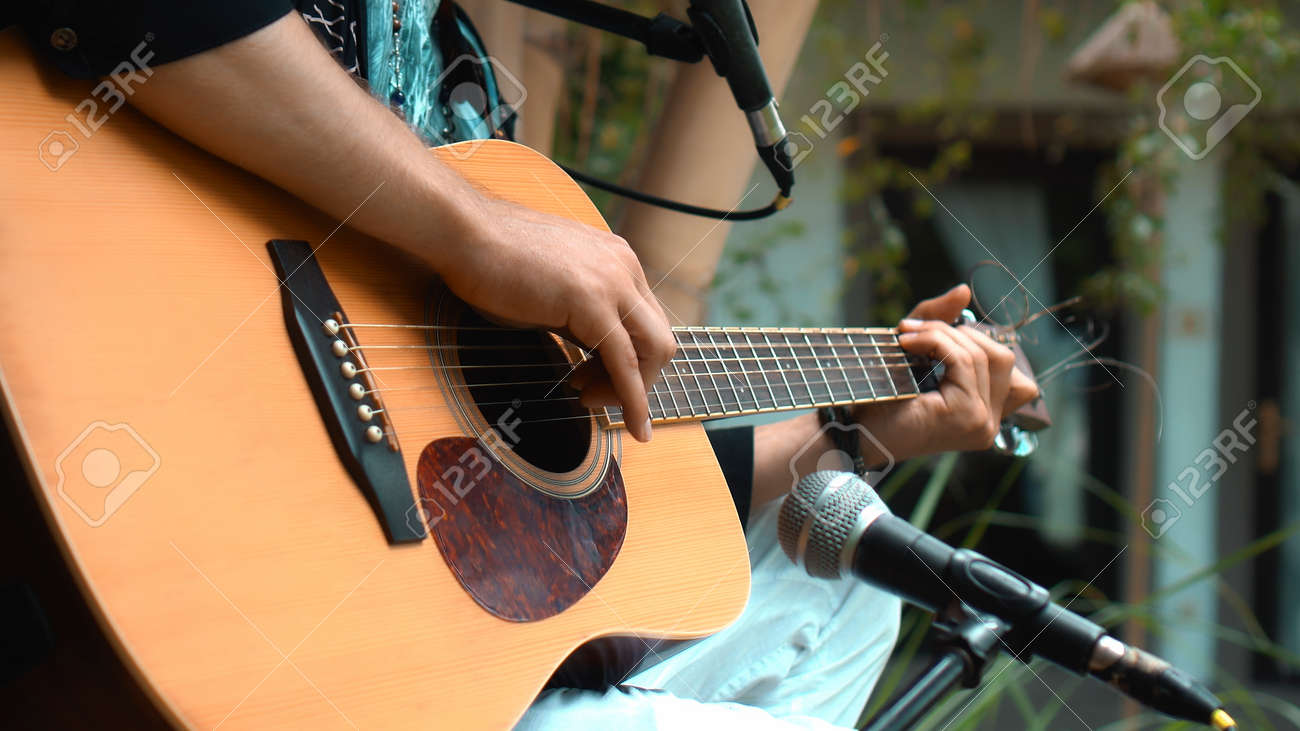 The young man plays hands and on a classic acoustic wooden guitar on the street using a microphone - 170790316 The young man plays hands and on a classic acoustic wooden guitar on the street using a microphone - 170790316