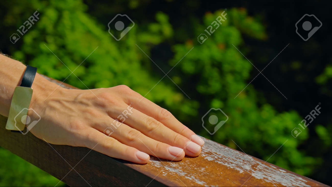 A young European girl stands in the summer on a balcony holding her hand to a wooden railing in a green dress - 171458630 A young European girl stands in the summer on a balcony holding her hand to a wooden railing in a green dress - 171458630