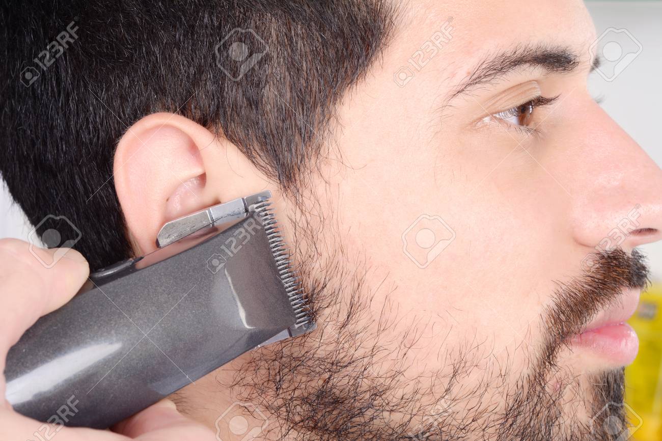 Close Up Of Young Man Having A Beard Cut With Hair Clippers Stock