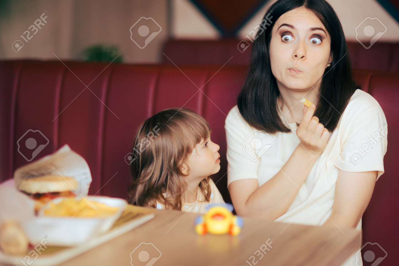 Funny Mom Having French Fries in front of her Toddler Daughter - 171549958 Funny Mom Having French Fries in front of her Toddler Daughter - 171549958