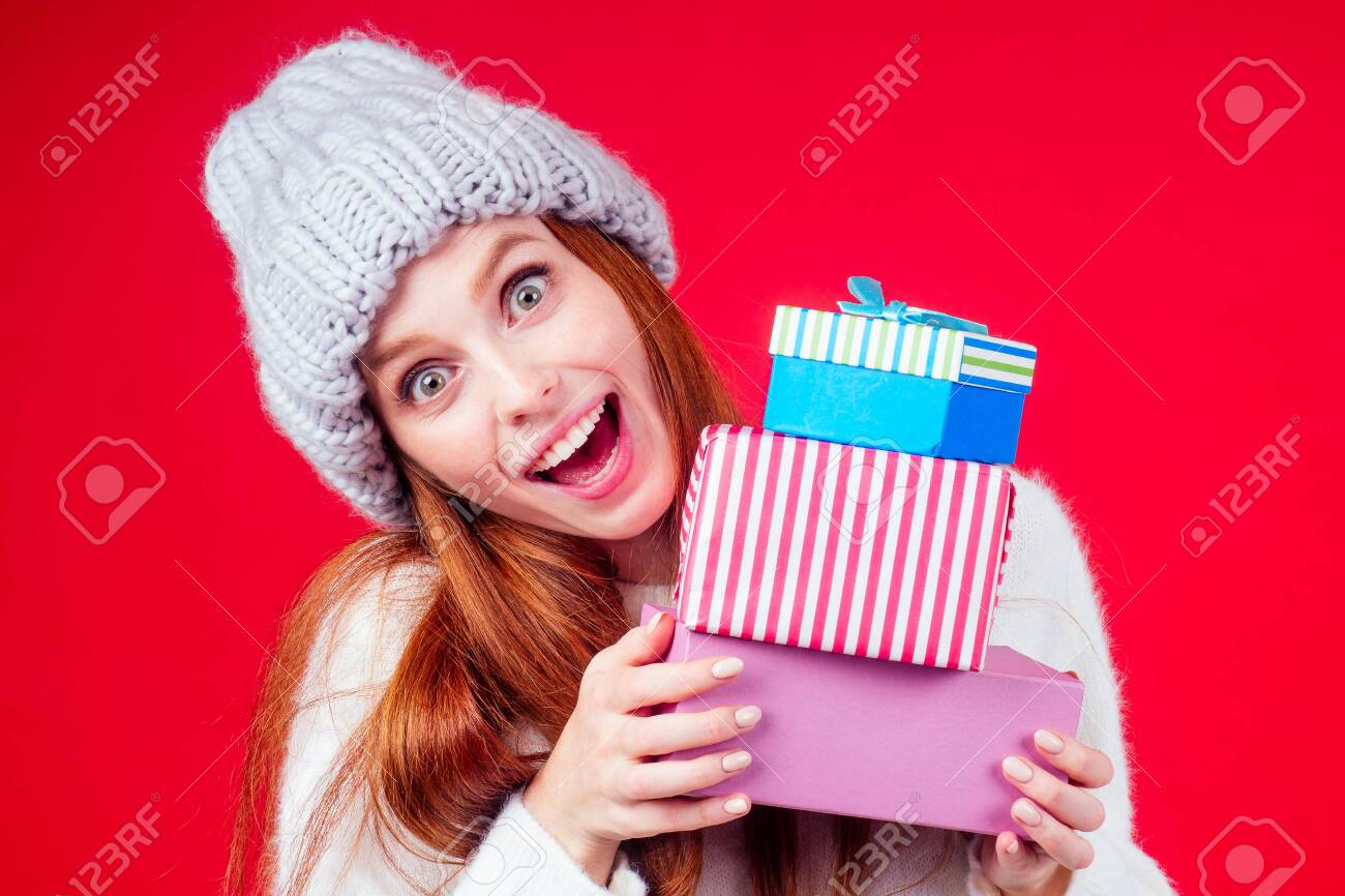 redhaired ginger woman wear stylish wool hat and white sweater looking at camera and hiding behind three boxes witg gifts copyspase in studio red background - 132847827 redhaired ginger woman wear stylish wool hat and white sweater looking at camera and hiding behind three boxes witg gifts copyspase in studio red background - 132847827