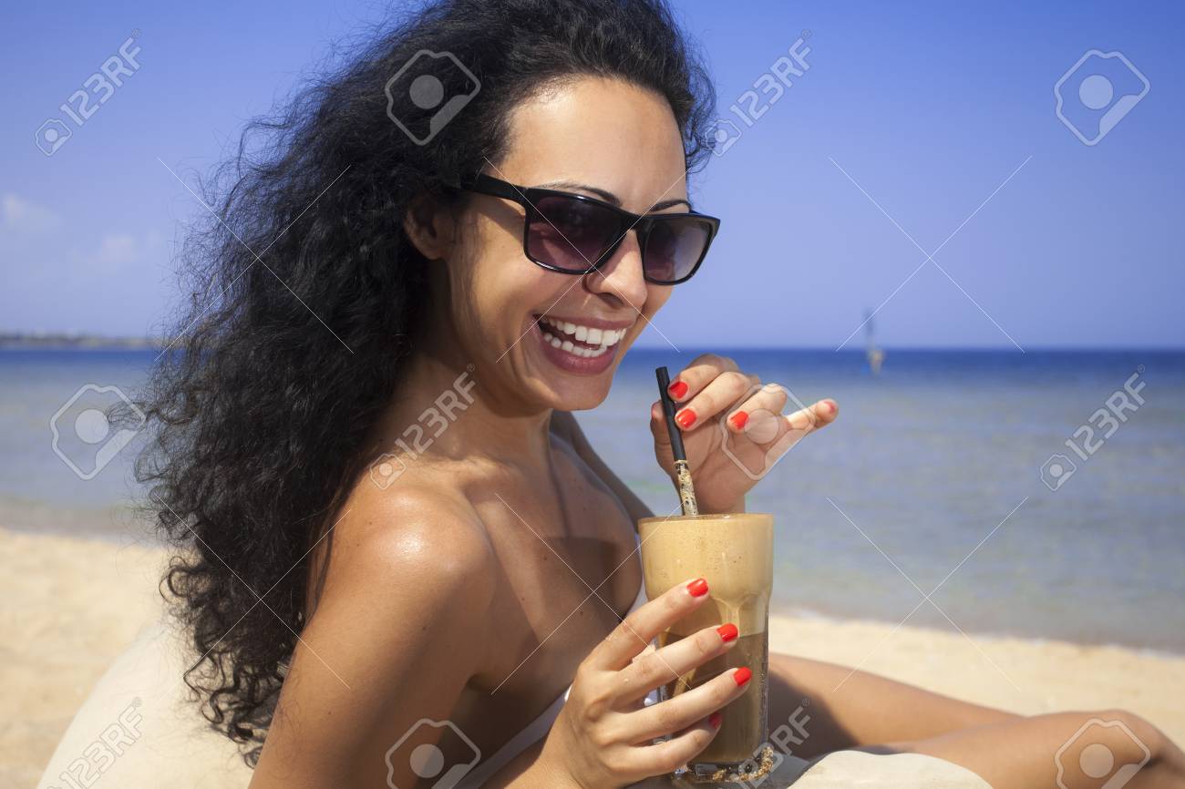 Young Beautiful Brunette Girl Drinking Iced Coffee On The Beach Young Beautiful Brunette Girl Drinking Iced Coffee On The Beach