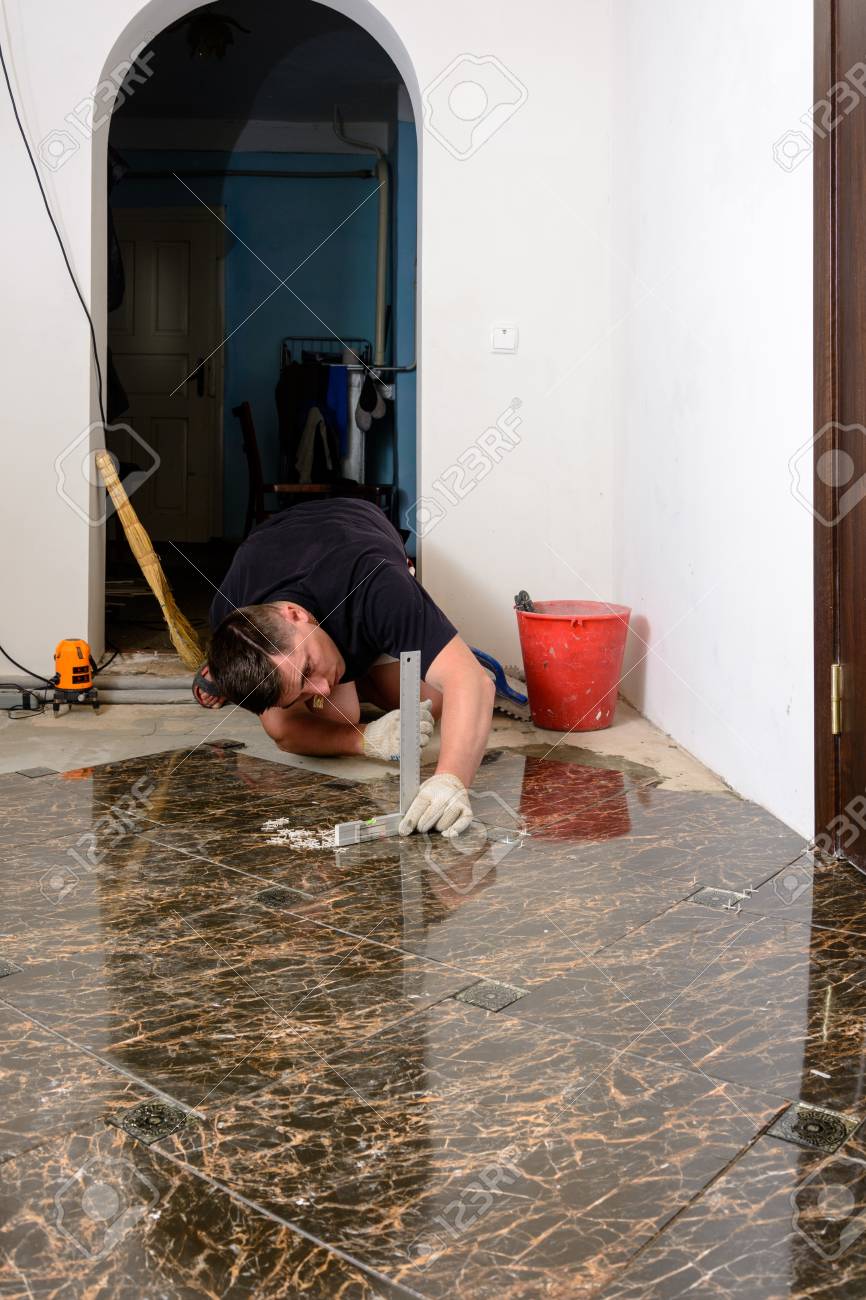 A Person With A Laser Level Checks The Installed Floor Tile Stock