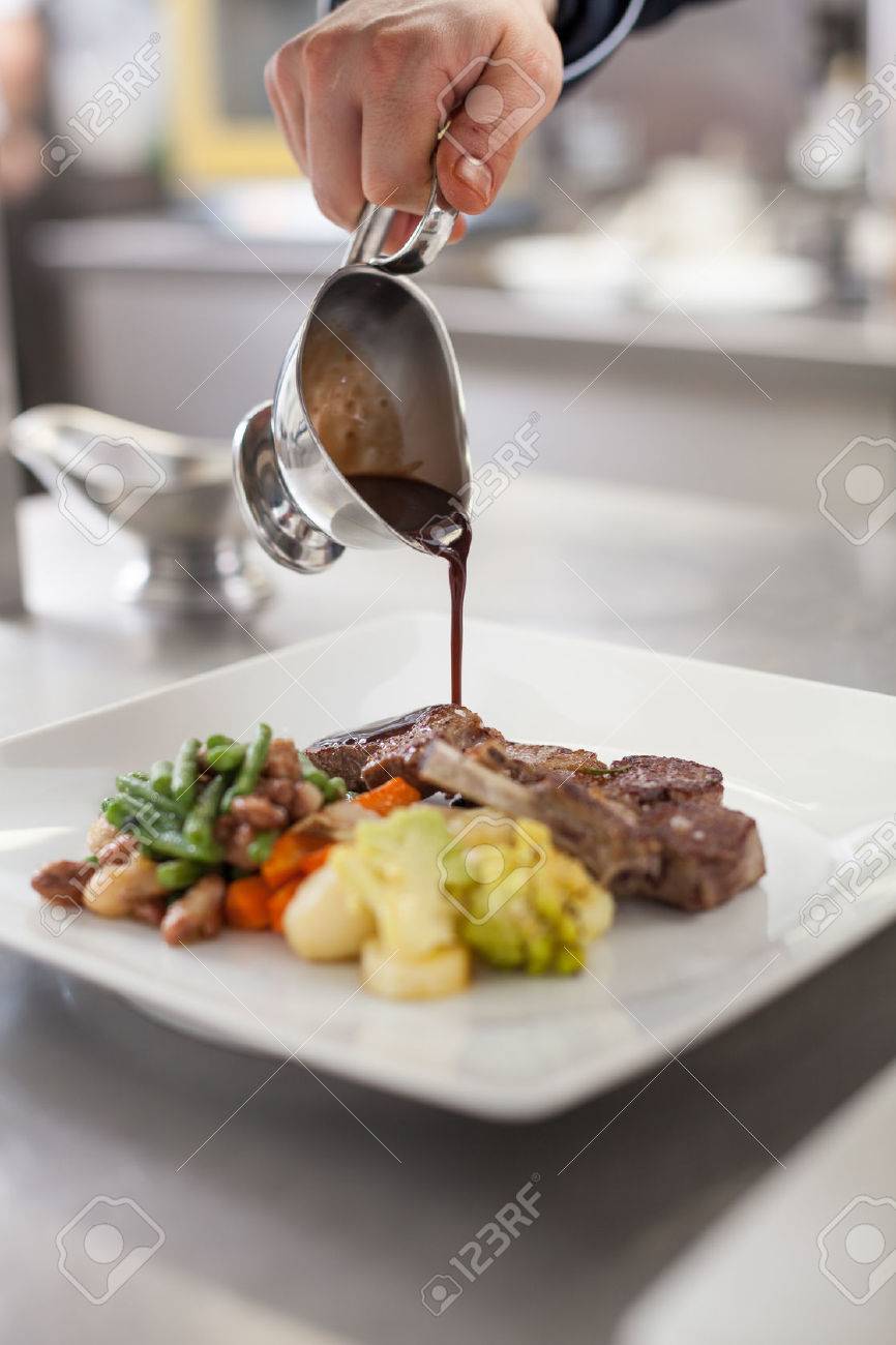 Chef plating up food in a restaurant pouring a gravy or sauce over the meat before
