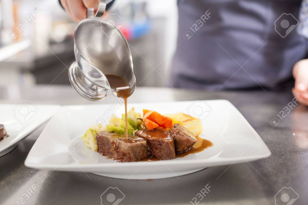 Chef plating up food in a restaurant pouring a gravy or sauce over the meat before