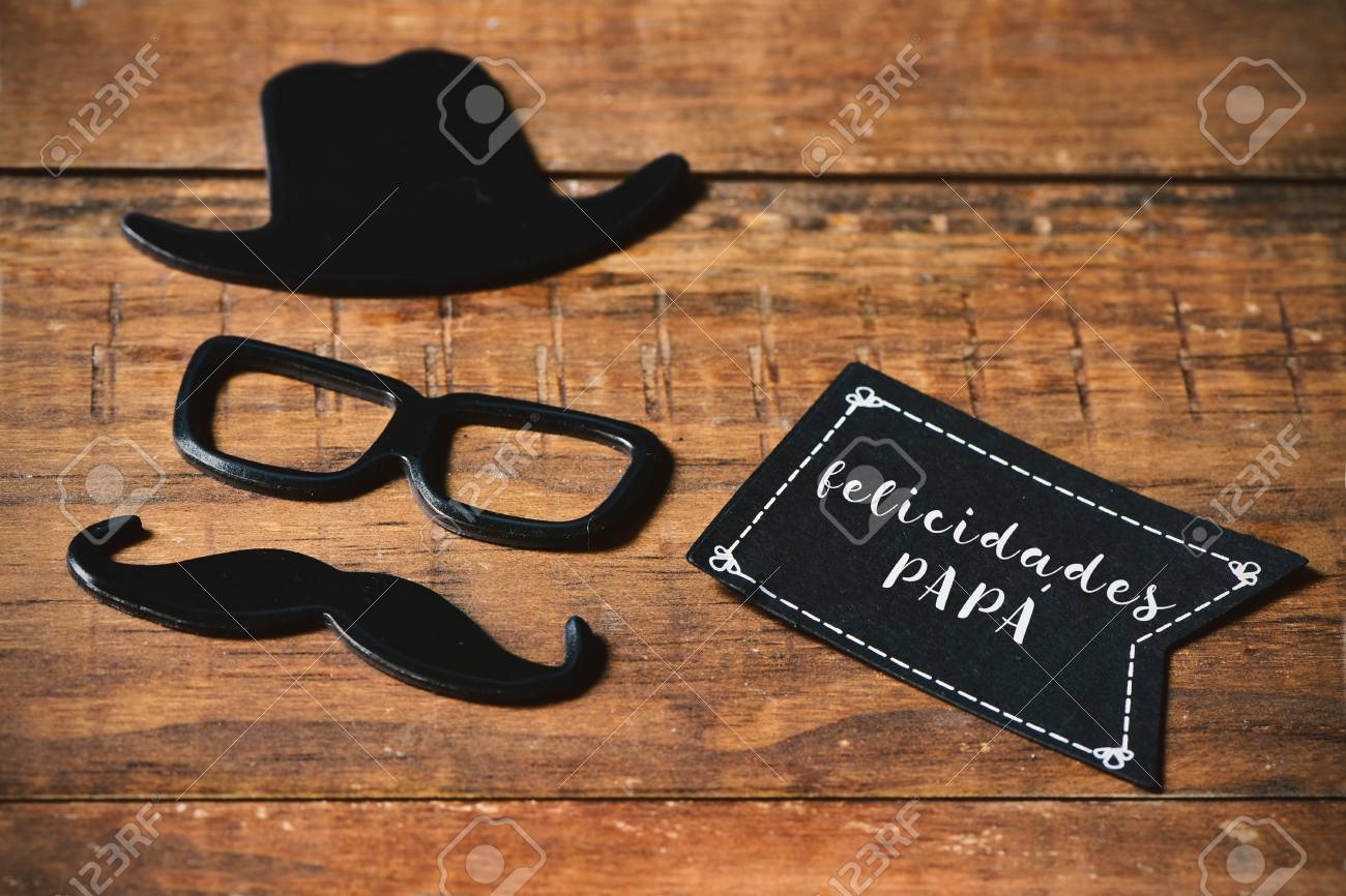 Eine Schwarze Flagge Formige Schild Mit Dem Text Felicidades Papa Gratulation Vater In Spanisch Und Einem Schnurrbart Einer Brille Und Einen Hut Das Gesicht Eines Mannes Auf Einem Rustikalen Holzoberflache Bildet Lizenzfreie