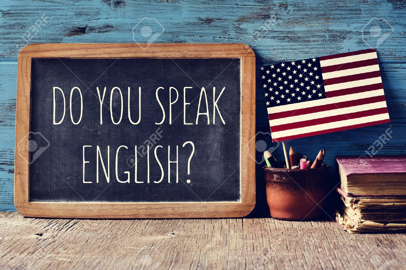 a chalkboard with the question do you speak English? written in it, a pot with pencils and the flag of the United States, on a wooden desk - 63892262 a chalkboard with the question do you speak English? written in it, a pot with pencils and the flag of the United States, on a wooden desk - 63892262