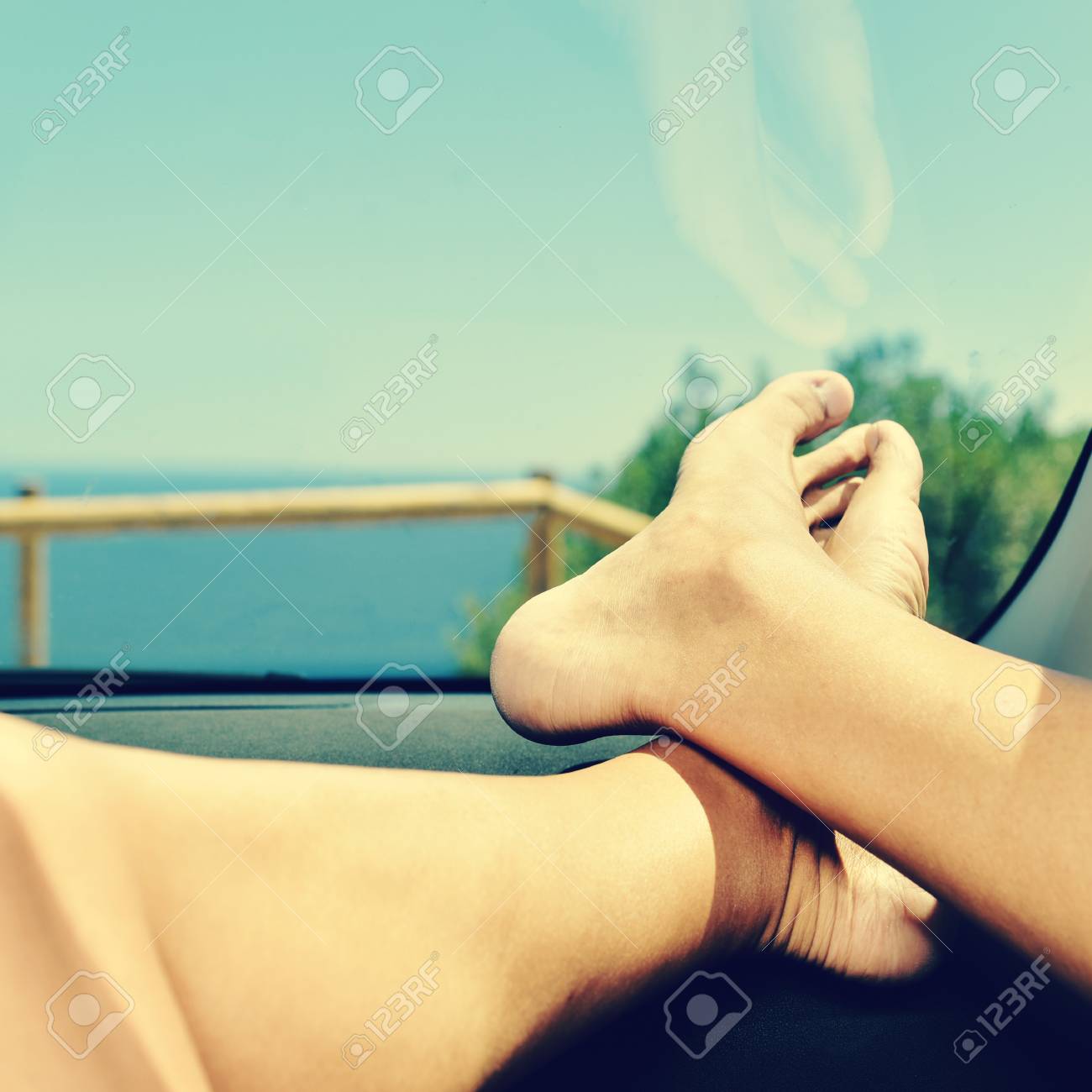 ダッシュ ボードで 海の近くの彼の裸の足が付いている車の助手席でリラックスする若い白人男のクローズ アップ の写真素材 画像素材 Image