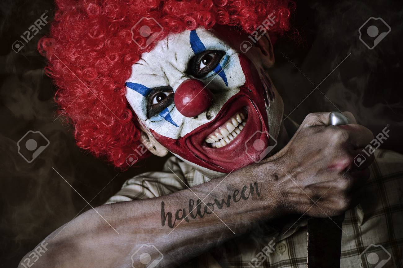 A Scary Evil Clown With A Big Knife In His Hand And The Word Halloween  Simulating A Tattoo In His Forearm, Against A Dark Background Stock Photo,  Picture and Royalty Free Image., image size:1300x866