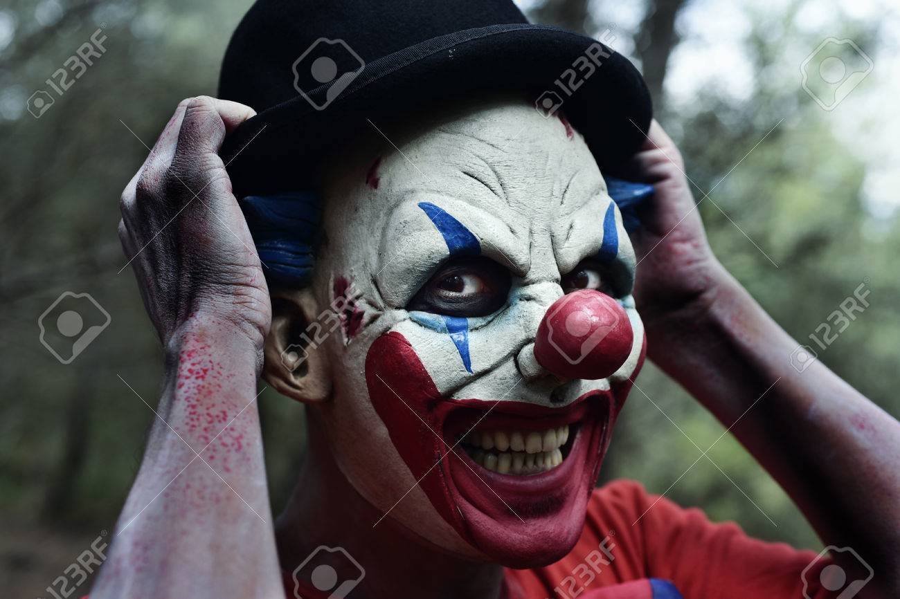 森の中の笑顔の中で怖い悪ピエロのクローズ アップは彼の山高帽を調整します の写真素材 画像素材 Image
