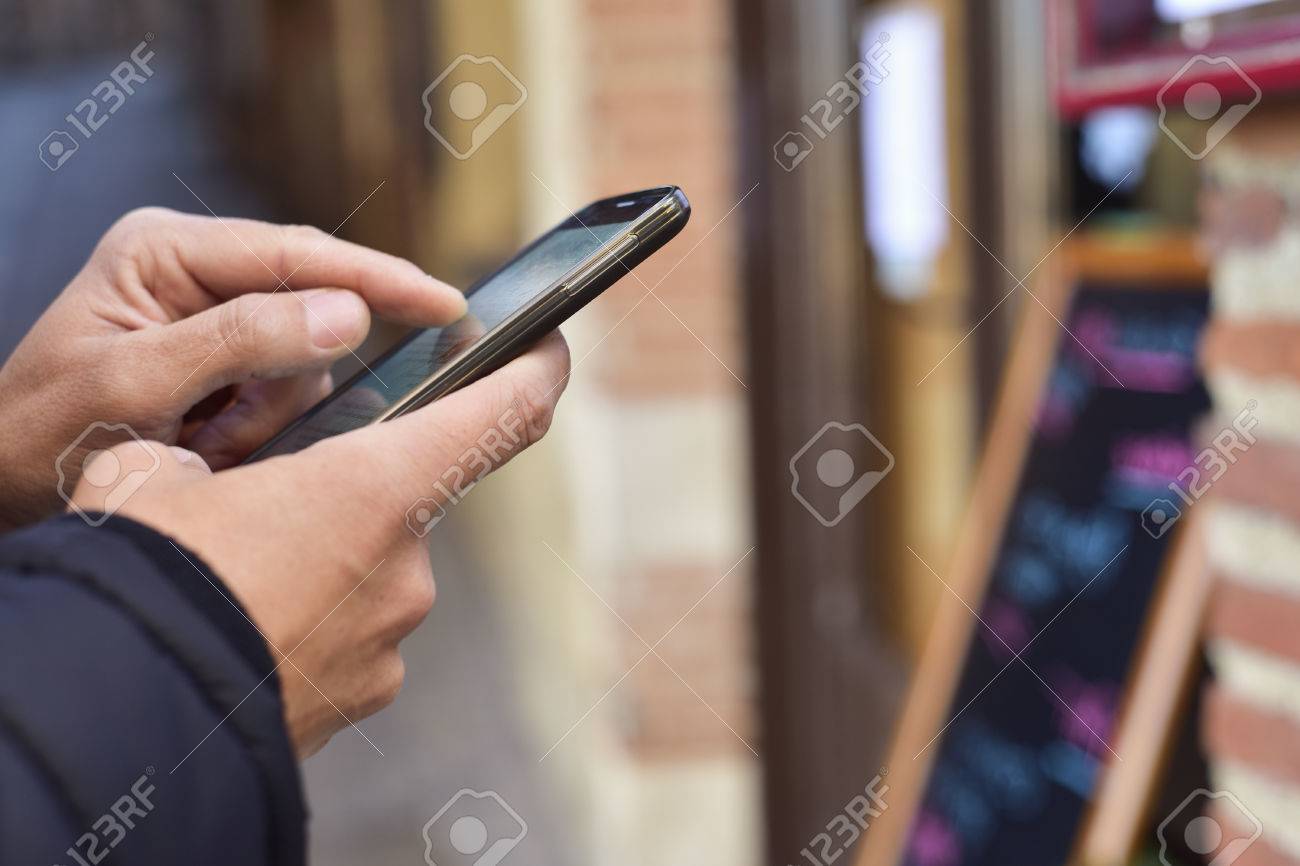 closeup of a young caucasian man using a smartphone in the street, in front of a restaurant - 70616757 closeup of a young caucasian man using a smartphone in the street, in front of a restaurant - 70616757