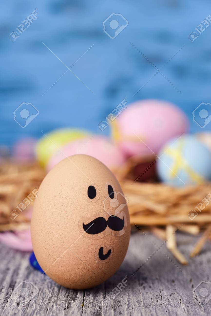 Closeup Of A Brown Egg With Funny Face On Rustic Wooden Surface And Some