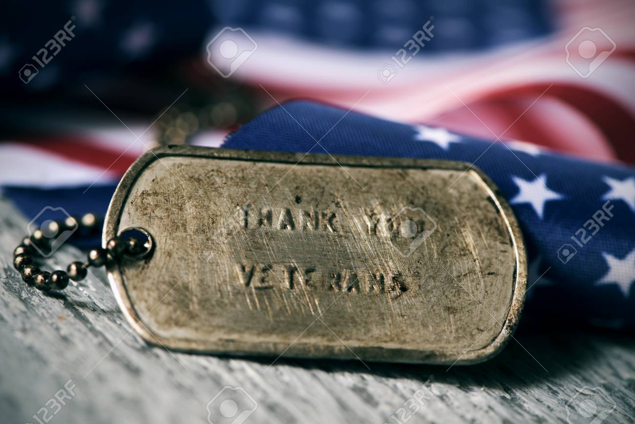 closeup of a rusty dog tag with the text thank you veterans engraved in it, next to a flag of the United States, on a rustic wooden surface - 89751270 closeup of a rusty dog tag with the text thank you veterans engraved in it, next to a flag of the United States, on a rustic wooden surface - 89751270